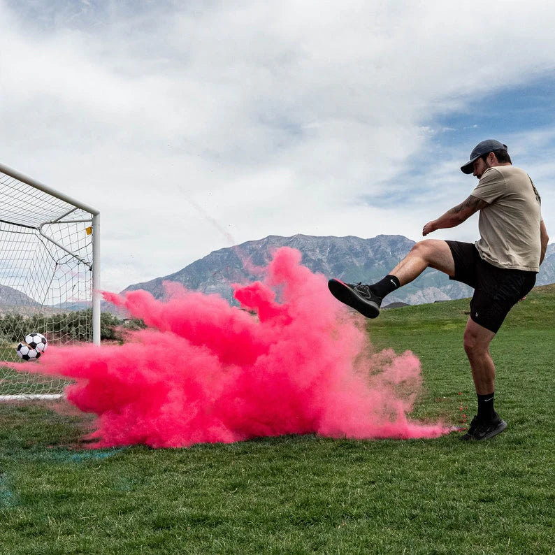 "Customer kicking pink powder-filled gender reveal soccer ball during outdoor football-themed baby reveal."